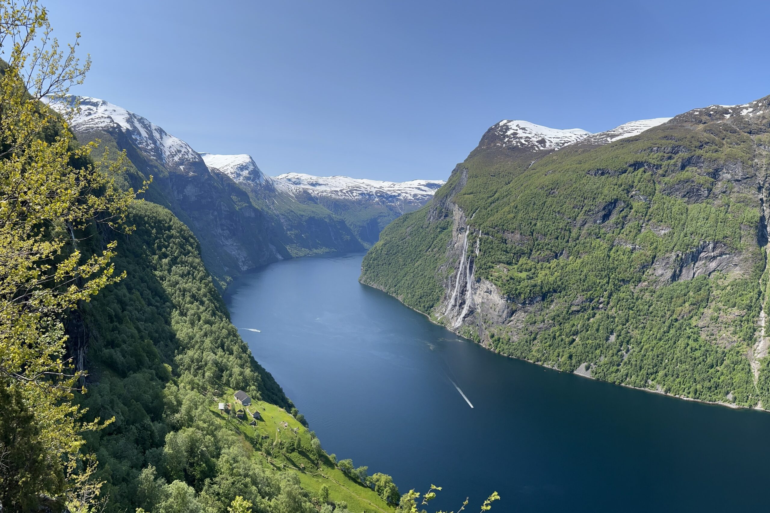 Geirangerfjord viewed from above — snow-capped mountains, deep blue water, cascading waterfalls